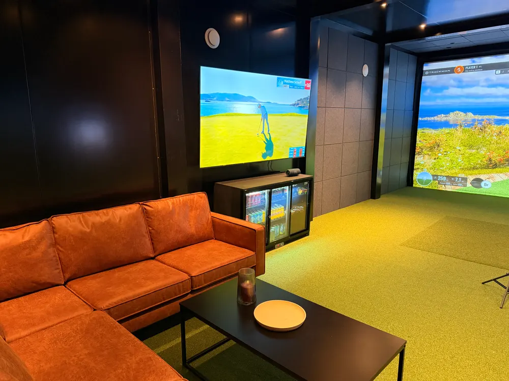 Loungen hos mer.golf med hjørnesofa, TV og simulatorskjerm